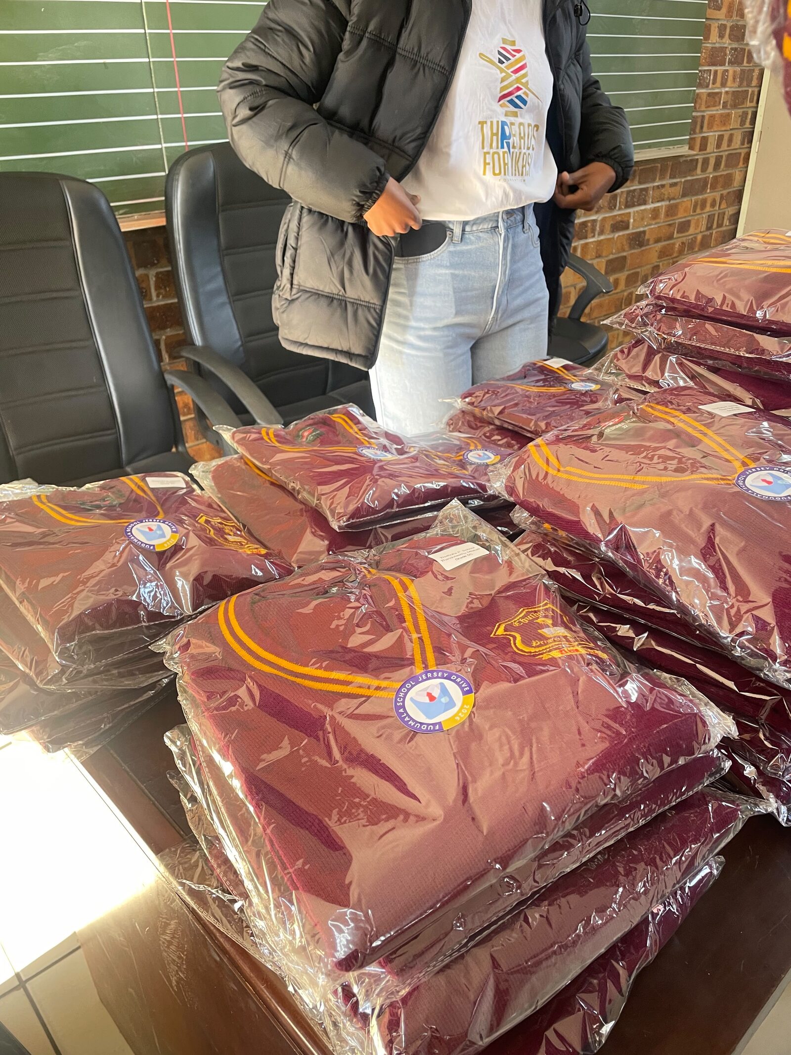 Stacks of sealed maroon Thuthuka Primary School jerseys, each carrying a Fudumala School Jersey Drive sticker and a learner's name label, 30 July 2026