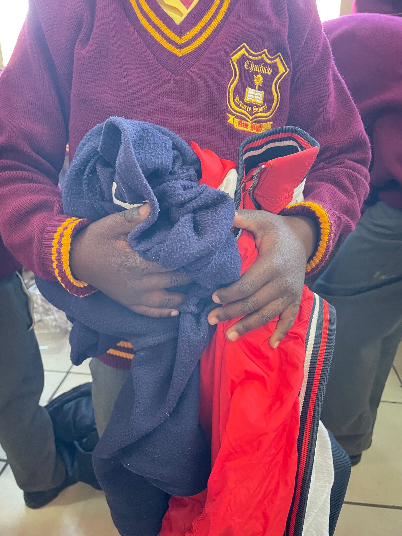 A Thuthuka Primary School learner holding a worn navy fleece and an old jacket at the handover, 30 July 2026