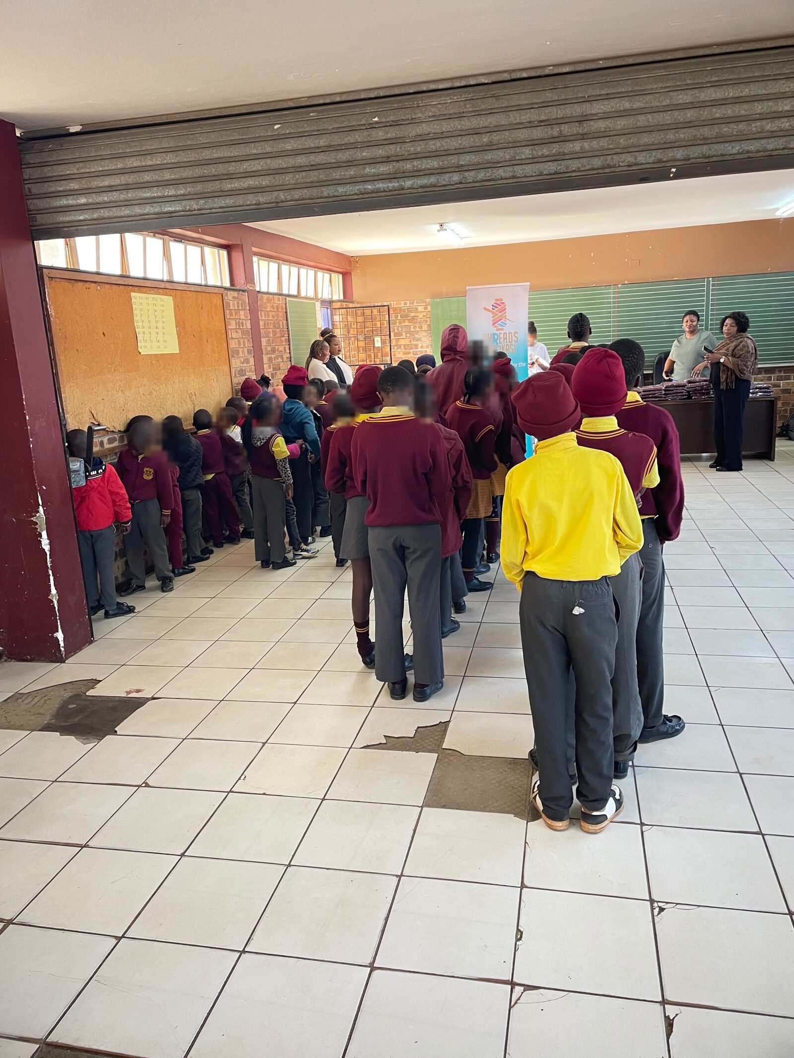 Thuthuka Primary School learners queuing along the school hall wall to collect their jerseys, 30 July 2026
